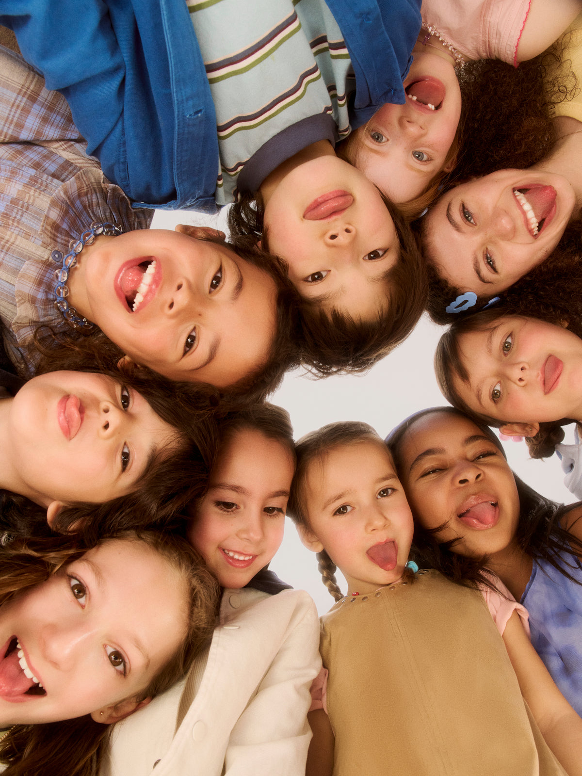 Group of diverse children and teens forming a circle, heads together, smiling and laughing at camera from below
