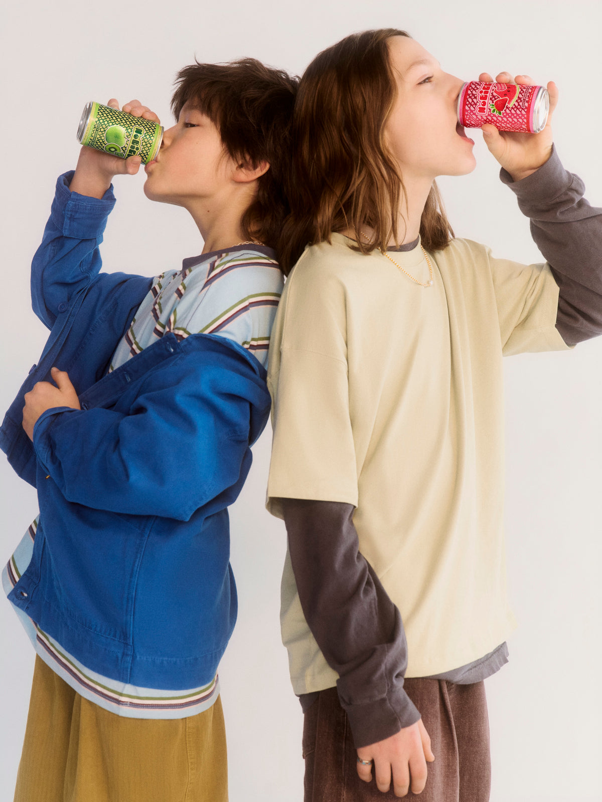 Two children drinking from colorful cans against a white background